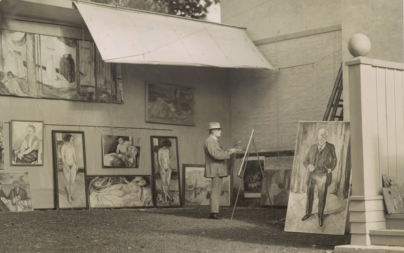 Edvard Munch står og maler i sitt friluftsatelier på Ekely. Han er omgitt av sine egne verk og har på seg en hatt som skygger for solen og en lys dress.