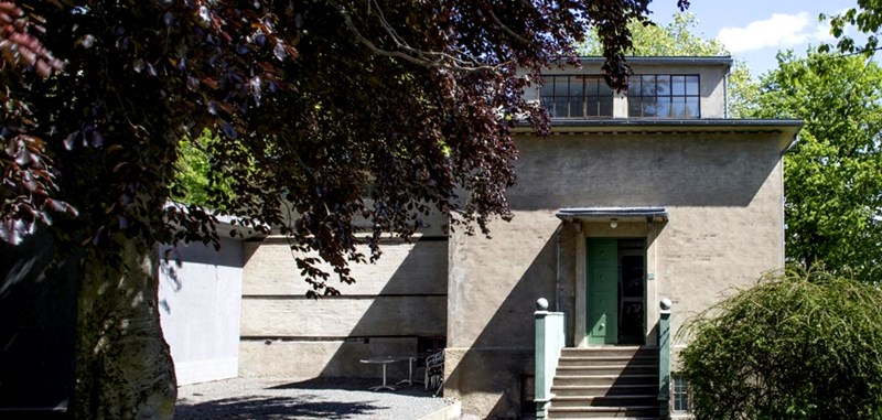 The winter studio at Ekely seen from the outside. A grey stone building with steps leading up to a green entrance door.