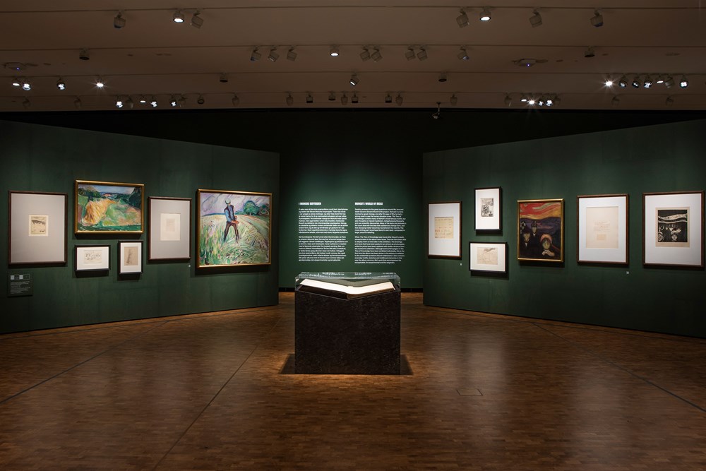 Photo from the exhibition All is Life. Edvard Munch's book The Tree of Knowledge is lying open on a pedestal in the middle of a green room. Other art works by Munch are displayed on the surrounding walls.