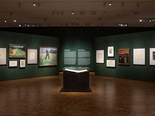 Photo from the exhibition All is Life. Edvard Munch's book The Tree of Knowledge is lying open on a pedestal in the middle of a green room. Other art works by Munch are displayed on the surrounding walls.