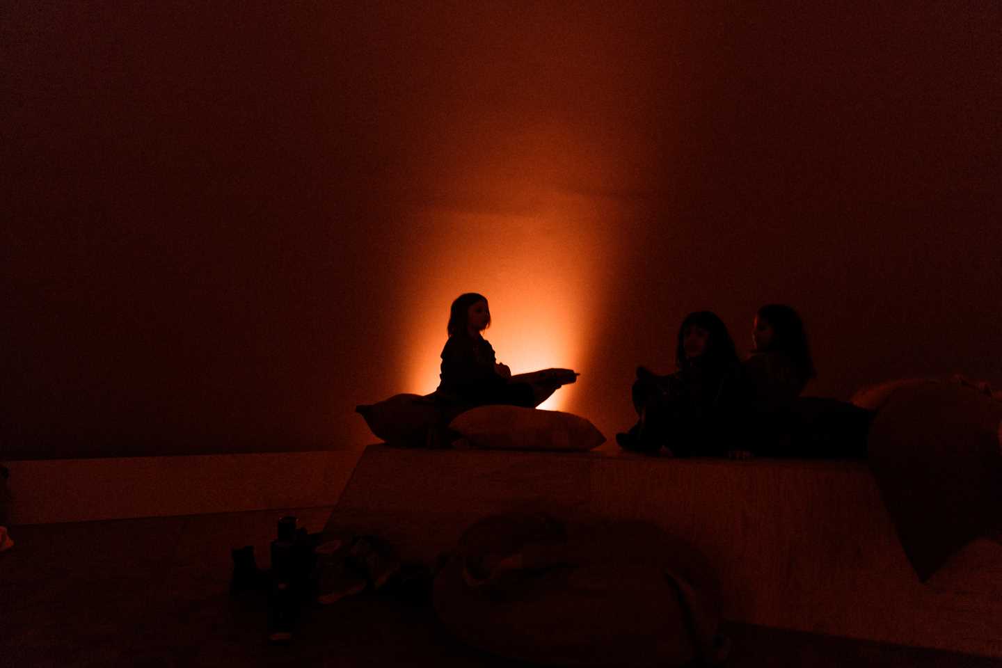 En stille stund i Kaoskammeret, med silhuetten av et barn som sitter på en pute i mørket, omgitt av et svakt oransje lys