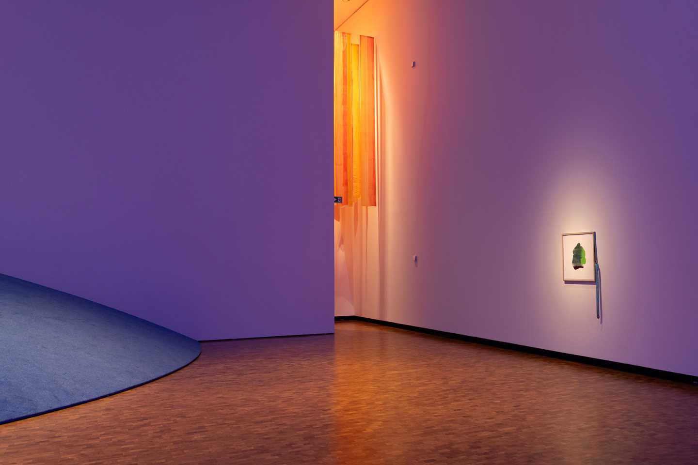 Deler av utstillingsrommet i flott fargespill med blått, lilla, oransje og gult. På den ene veggen henger et kunstverk. Fotografi