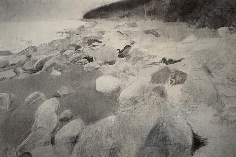 En hvit og steinete strand går i en slak bue innover i bildet. I bakgrunnen ser vi mørkt fjell som stiger opp fra stranden.