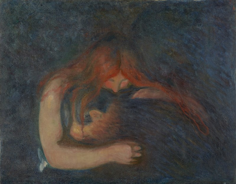 A man buries his head in a woman’s lap. She embraces him, placing her mouth on the back of his neck. Her blood-red hair is draped around the man’s body. The room around them is dark. 